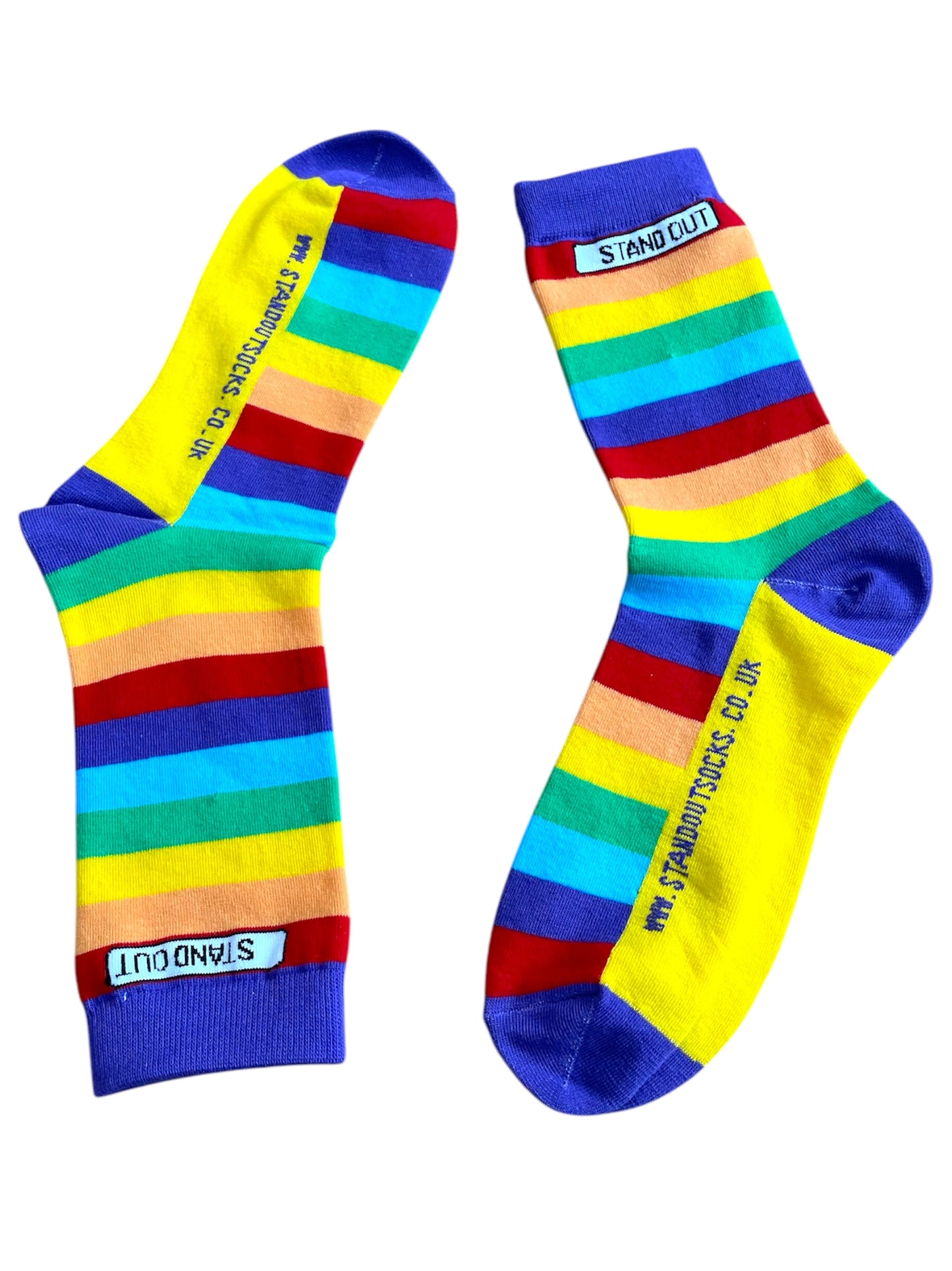 A photograph of a pair of Stand Out Socks Rainbow Pride design, showcasing vibrant rainbow stripes and the Stand Out logo near the cuff and website on the foot.