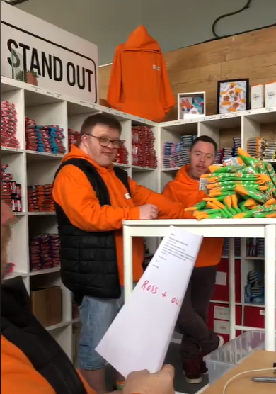 Ross and Oliver Standing at Table with Socks as Christian reads them customer feedback