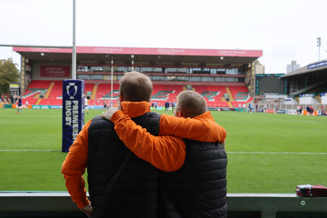 2 men stood at a rugy field with arms around each other 