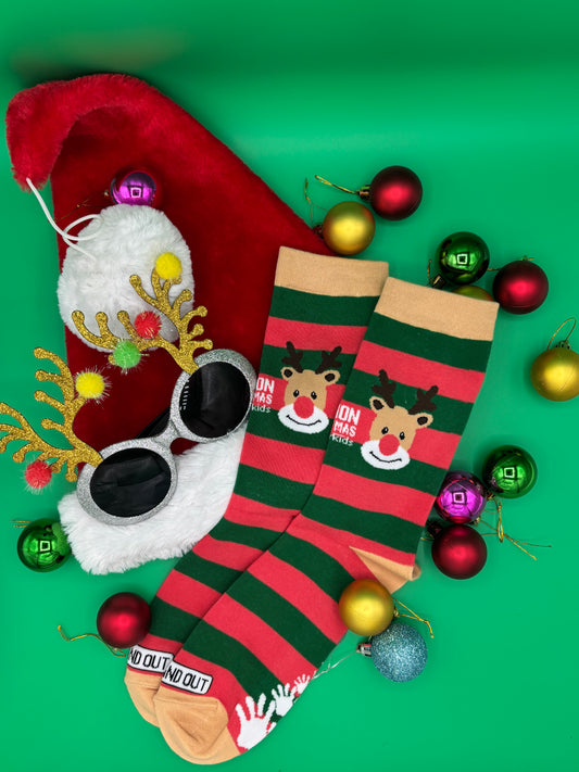 Red and green striped socks with reindeer design, sunglasses, and Christmas ornaments on a green background