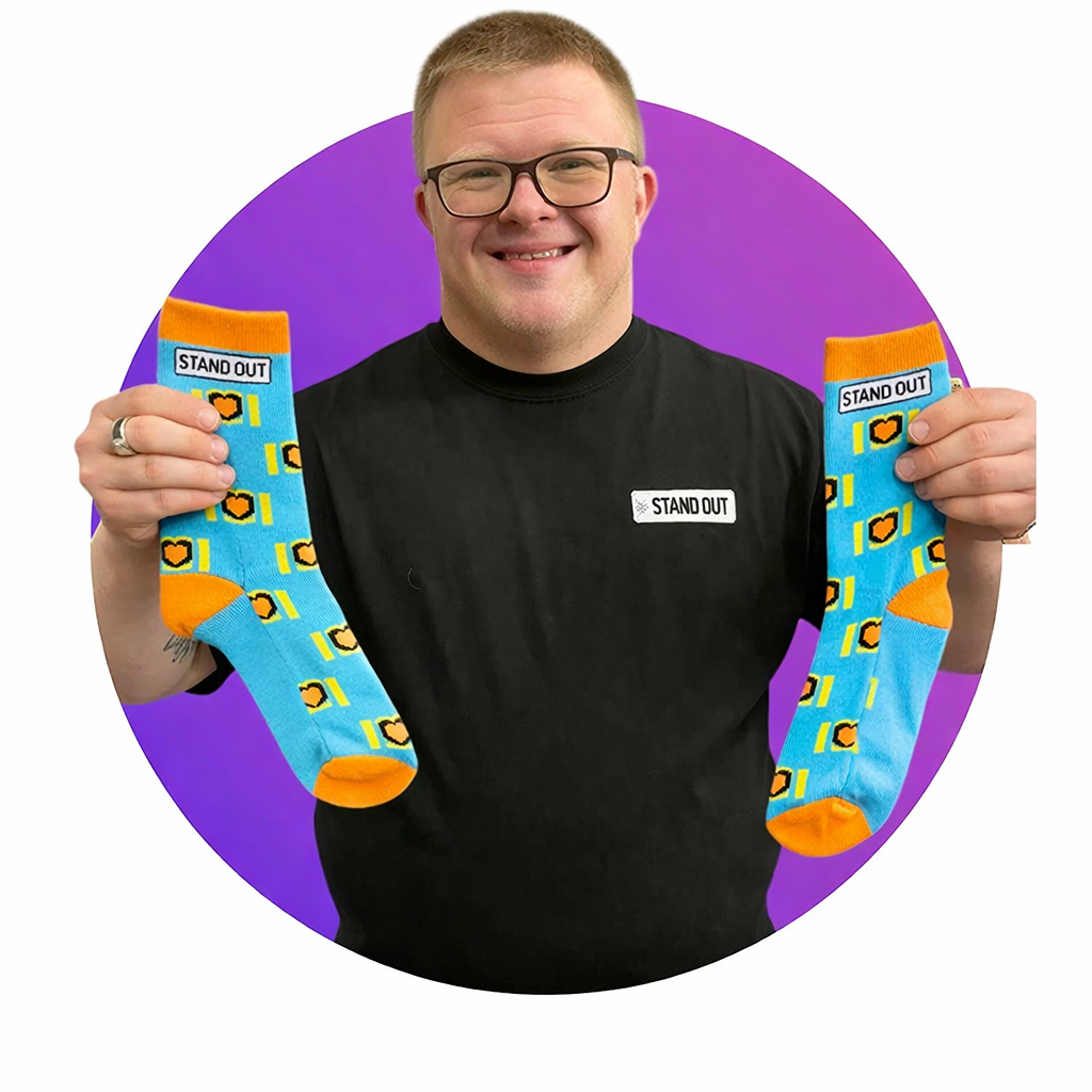 Man holding blue socks with orange accents and 'Stand Out' branding against a purple background