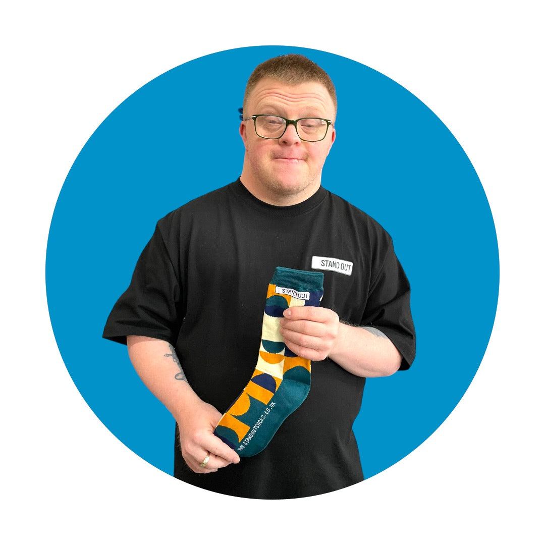 A Man holding up a Geometric Patterned socks and smiling. There is a Blue circle frame around the picture. 