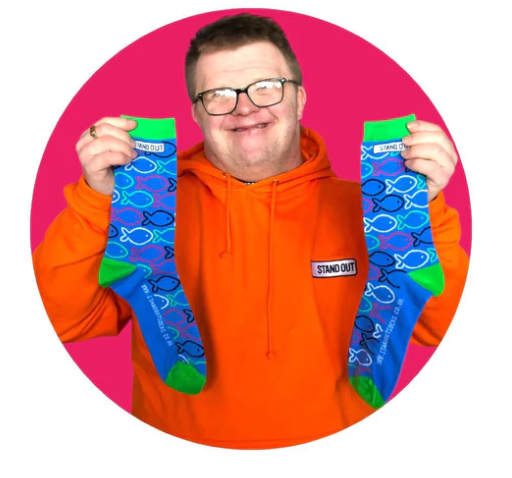 a man with glasses on smiling and holding some fish pattern socks with a pink circle frame around him