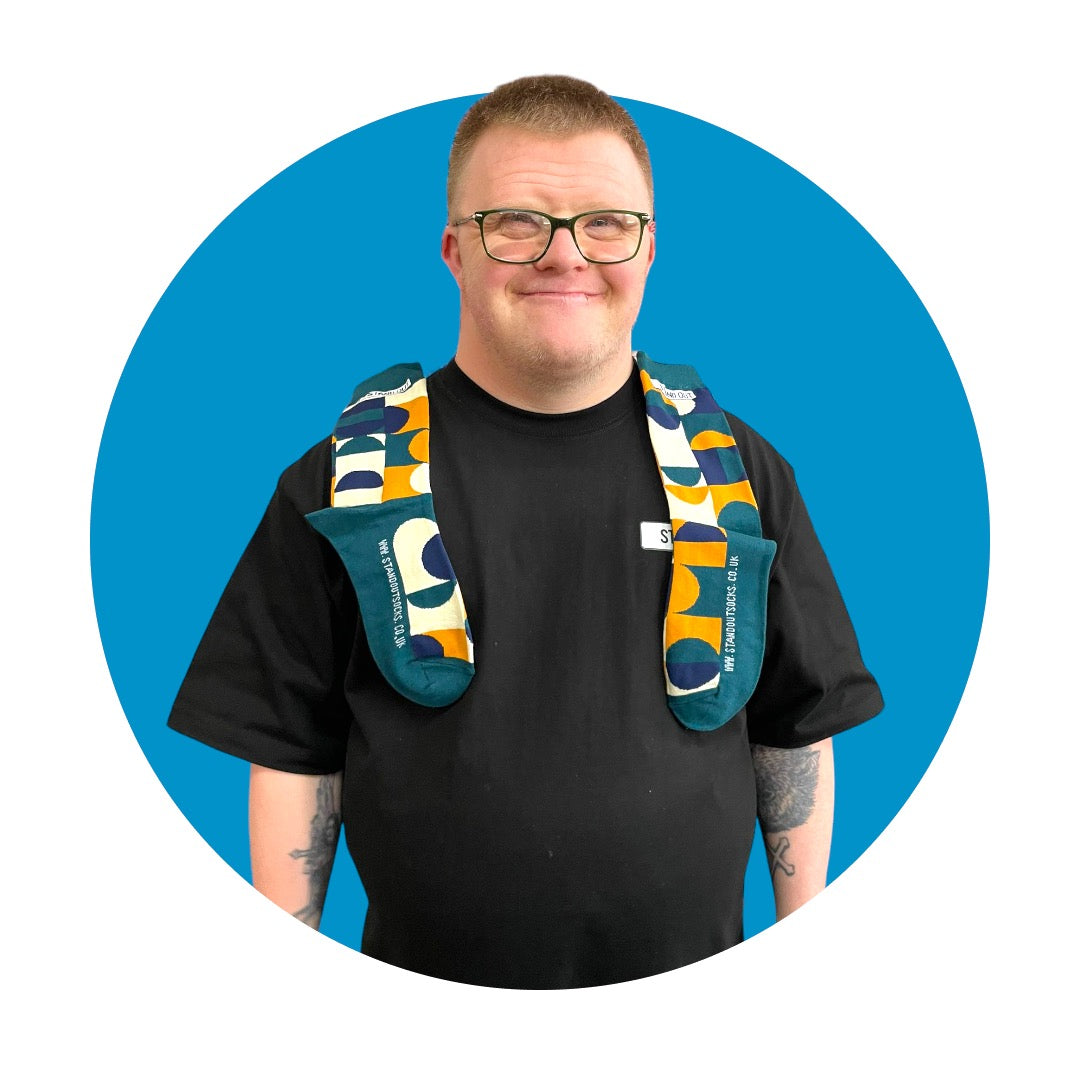 A Man with a pair Geometric Patterned socks lay over his shoulders and the man is smiling. There is a Blue circle frame around the picture. 