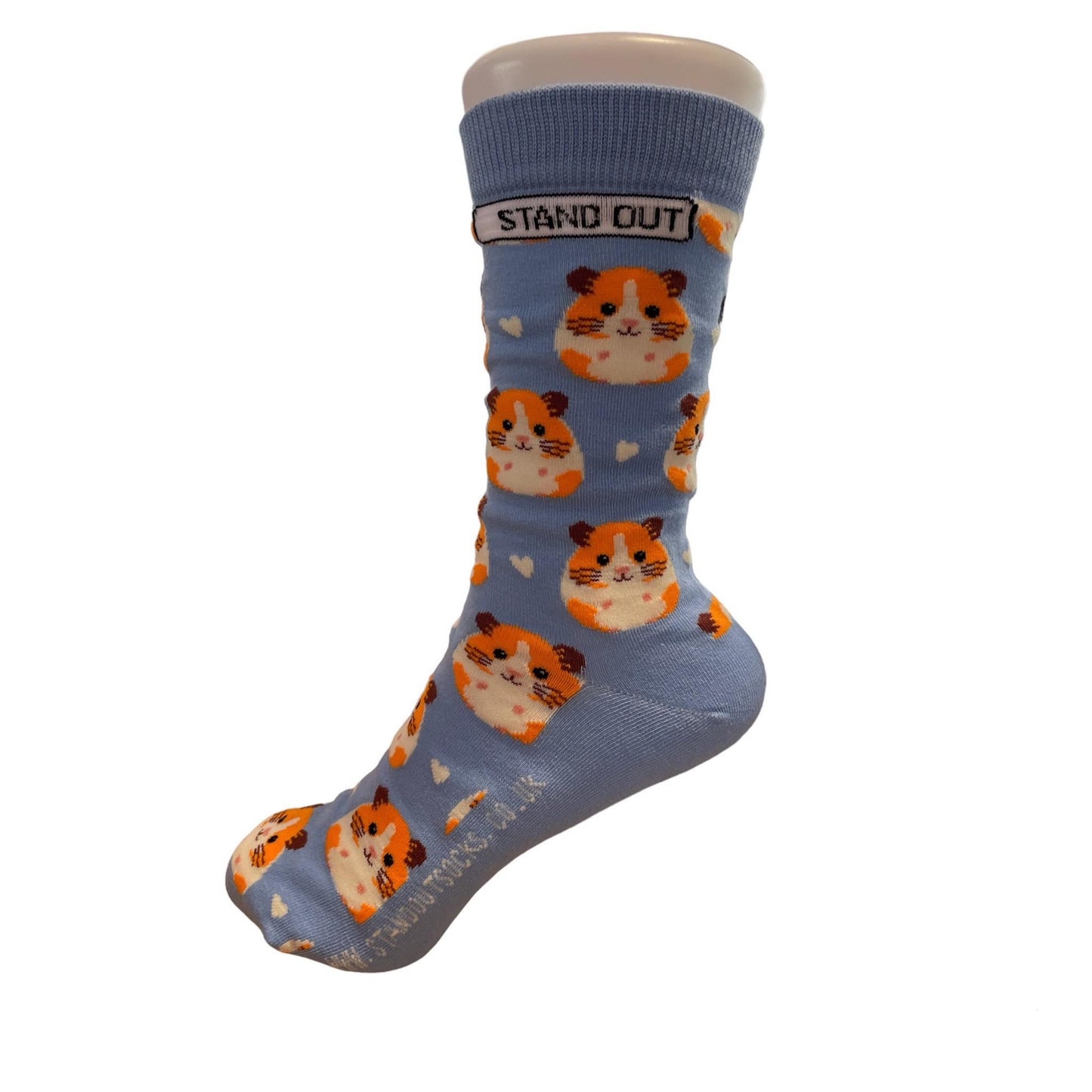 Light blue socks featuring a cute guinea pig pattern, created by Stand Out Socks. The socks display a playful design with orange and white hamster faces and small white hearts scattered throughout. The words "STAND OUT" are visible on the cuff and the company's website is printed on the sole.